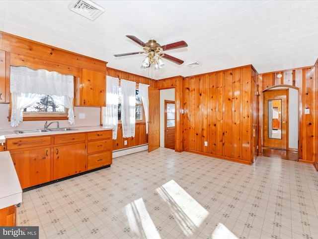 kitchen featuring baseboard heating, wooden walls, sink, and ceiling fan