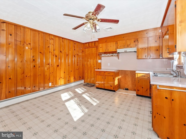 kitchen with baseboard heating, wood walls, sink, and ceiling fan