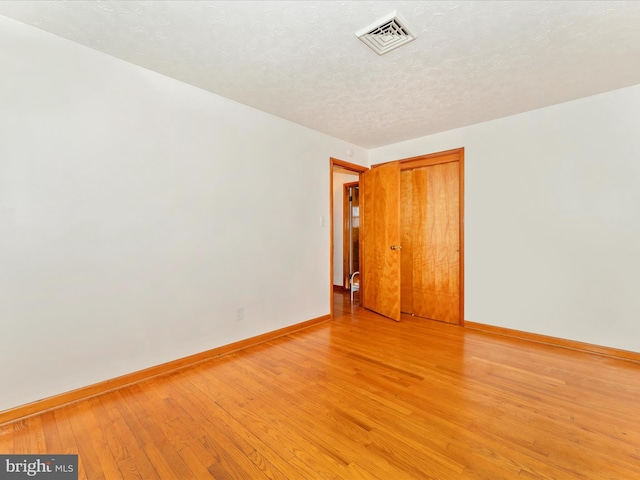 spare room featuring a textured ceiling and light hardwood / wood-style flooring