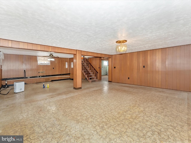 basement with a textured ceiling, wooden walls, ceiling fan with notable chandelier, and a baseboard heating unit