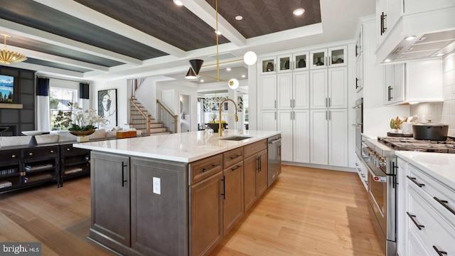 kitchen featuring premium range hood, stainless steel appliances, sink, a center island with sink, and white cabinetry