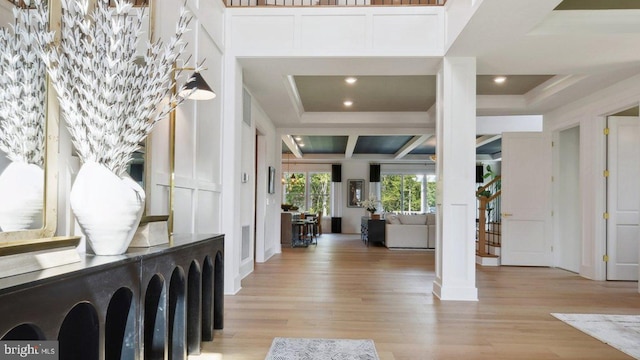 foyer entrance featuring light wood-type flooring, ornate columns, and coffered ceiling