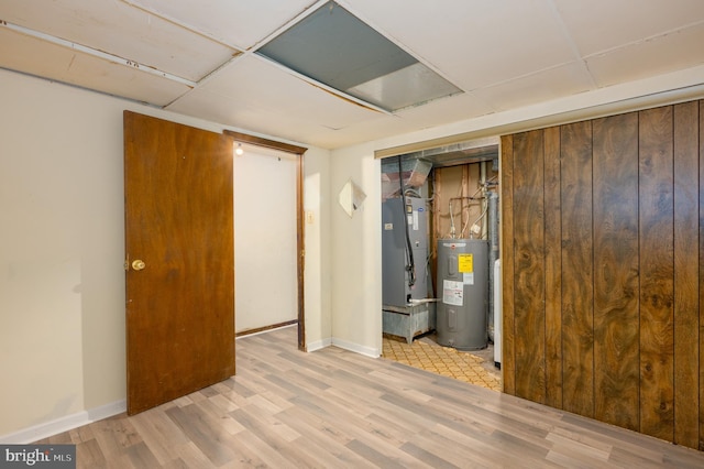 basement featuring heating unit, electric water heater, a paneled ceiling, and light wood-type flooring