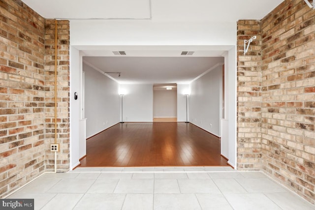 tiled empty room with brick wall, visible vents, and crown molding