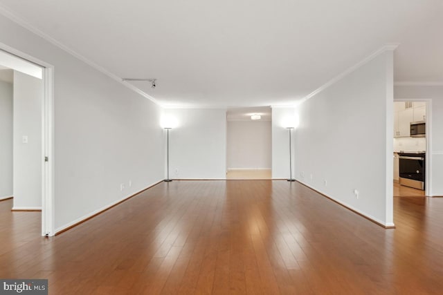 empty room with baseboards, wood-type flooring, and crown molding