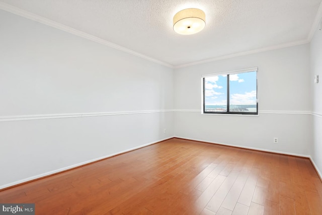 empty room featuring a textured ceiling, baseboards, wood finished floors, and ornamental molding