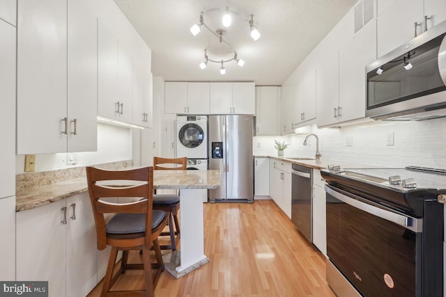 kitchen featuring appliances with stainless steel finishes, stacked washer and clothes dryer, and white cabinetry