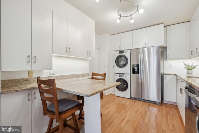 kitchen featuring stacked washer and clothes dryer, light wood-style flooring, appliances with stainless steel finishes, a kitchen breakfast bar, and white cabinetry