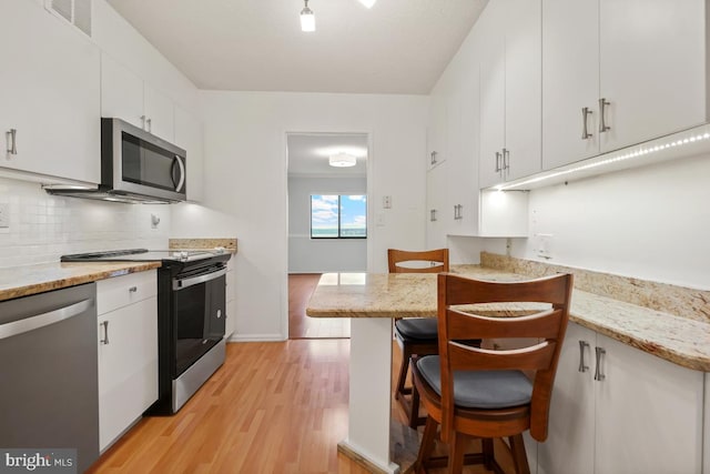 kitchen with visible vents, decorative backsplash, appliances with stainless steel finishes, light wood-style floors, and a kitchen bar