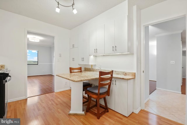 kitchen featuring white cabinets, light wood finished floors, a breakfast bar area, and a peninsula