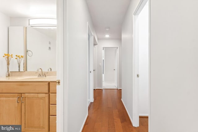 corridor with light wood-style floors, a sink, and baseboards