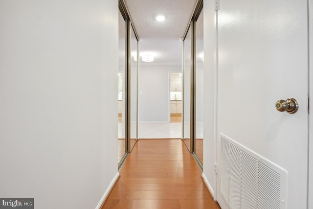 hall featuring light wood-type flooring, baseboards, visible vents, and a textured ceiling