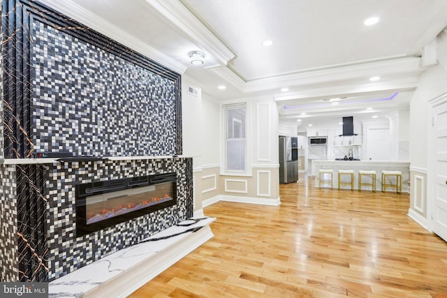 living room featuring hardwood / wood-style flooring, a raised ceiling, crown molding, and a tiled fireplace