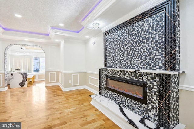 living room with a tile fireplace, wood-type flooring, a tray ceiling, and ornamental molding