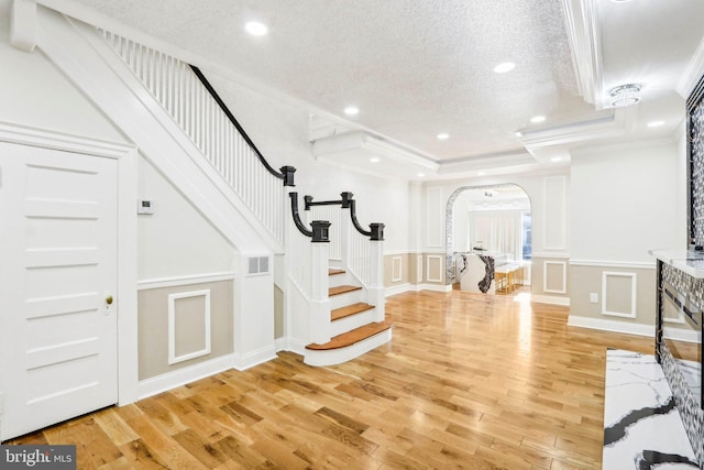 foyer with a tray ceiling, crown molding, light hardwood / wood-style flooring, and a textured ceiling