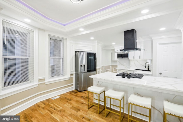 kitchen with white cabinets, light hardwood / wood-style floors, appliances with stainless steel finishes, island range hood, and light stone counters