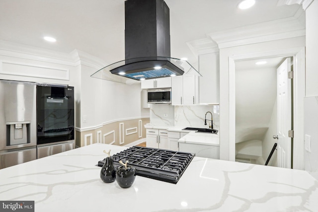 kitchen with island exhaust hood, appliances with stainless steel finishes, light stone countertops, crown molding, and white cabinetry