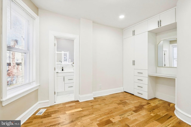 unfurnished bedroom with ensuite bathroom and light hardwood / wood-style flooring