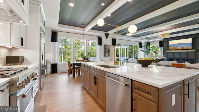 kitchen with sink, stainless steel appliances, decorative light fixtures, white cabinets, and light wood-type flooring