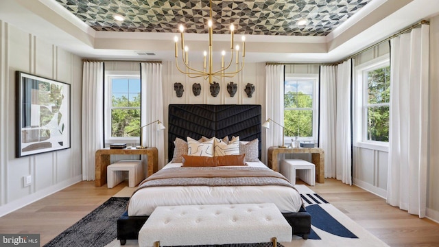 bedroom featuring light wood-type flooring, a tray ceiling, and multiple windows