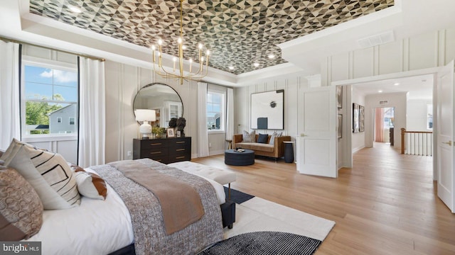 bedroom featuring an inviting chandelier, a raised ceiling, multiple windows, and light hardwood / wood-style flooring