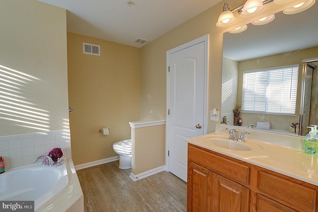 bathroom featuring wood-type flooring, vanity, tiled bath, and toilet