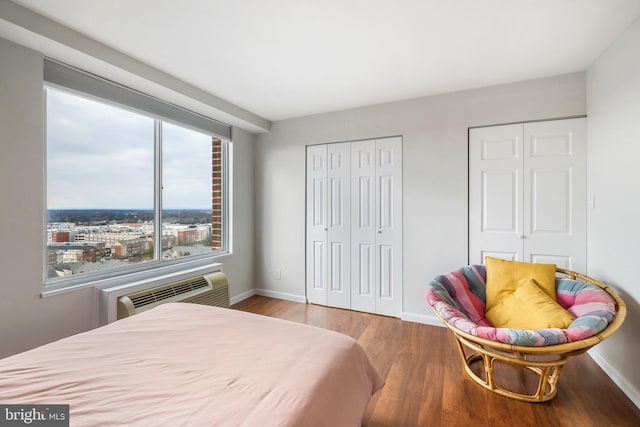 bedroom with a wall mounted air conditioner, hardwood / wood-style floors, and multiple closets