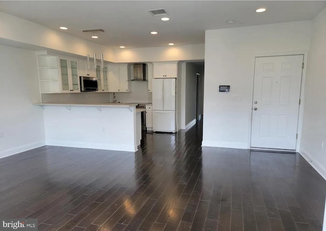 kitchen with white fridge, a breakfast bar, kitchen peninsula, white cabinetry, and wall chimney exhaust hood