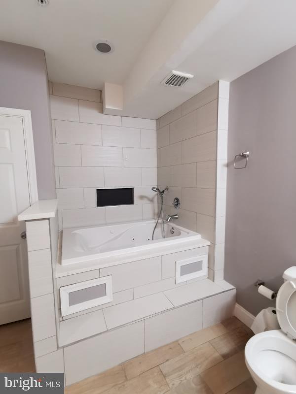 bathroom featuring tiled bath, toilet, and tile patterned flooring