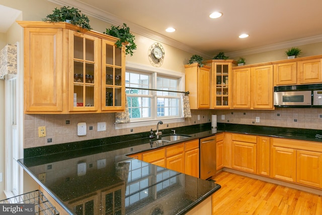 kitchen featuring sink, dark stone countertops, ornamental molding, stainless steel appliances, and light wood-type flooring