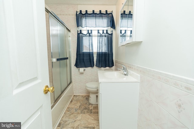 full bathroom with vanity, toilet, tile walls, and bath / shower combo with glass door