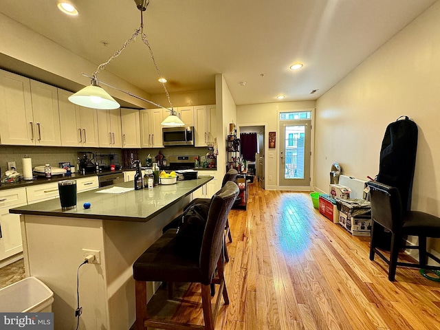 kitchen with a center island, hanging light fixtures, stainless steel appliances, light hardwood / wood-style flooring, and white cabinets