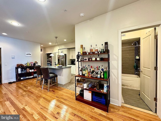 bar with stainless steel fridge, light hardwood / wood-style flooring, and hanging light fixtures