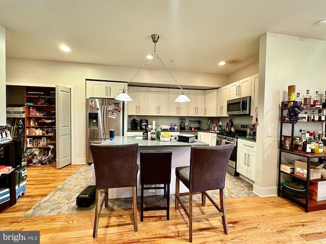 kitchen with light wood-type flooring, hanging light fixtures, appliances with stainless steel finishes, and a breakfast bar area