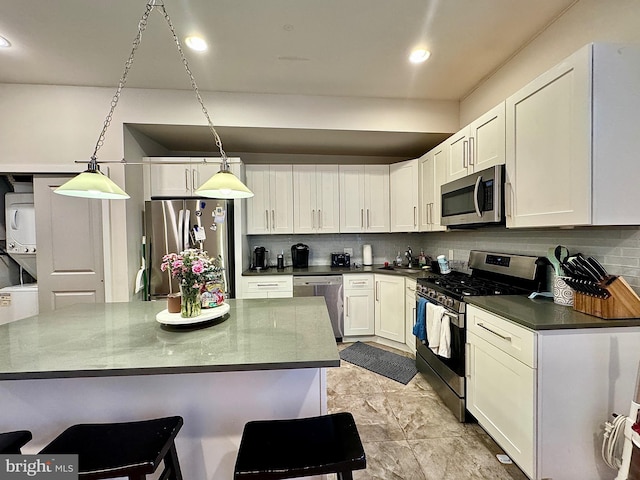 kitchen with tasteful backsplash, stacked washer / dryer, decorative light fixtures, white cabinets, and appliances with stainless steel finishes