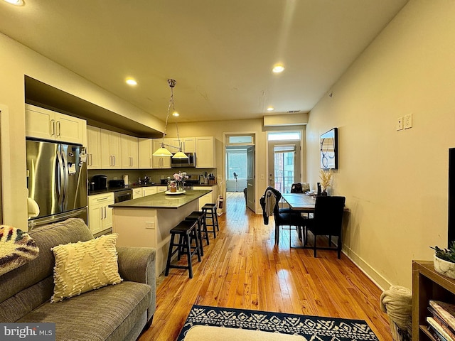 kitchen with stainless steel appliances, a kitchen island, white cabinetry, and a breakfast bar area