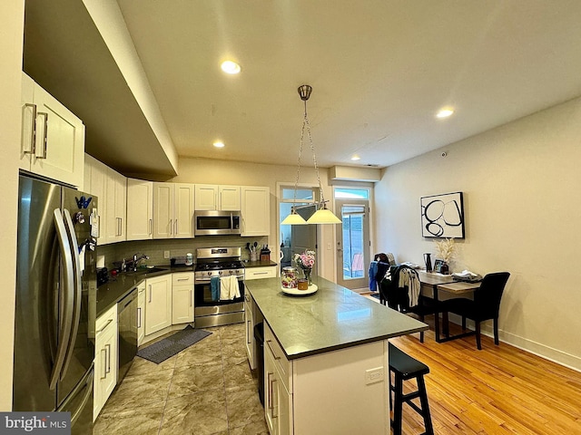 kitchen with white cabinetry, a center island, hanging light fixtures, appliances with stainless steel finishes, and light wood-type flooring