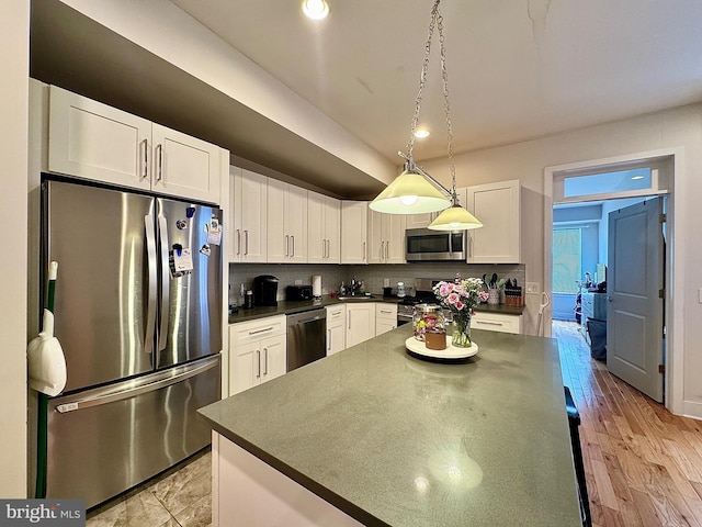 kitchen featuring light wood-type flooring, backsplash, stainless steel appliances, pendant lighting, and white cabinetry