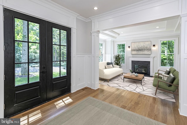 foyer entrance featuring french doors, light hardwood / wood-style flooring, ornamental molding, a tray ceiling, and decorative columns