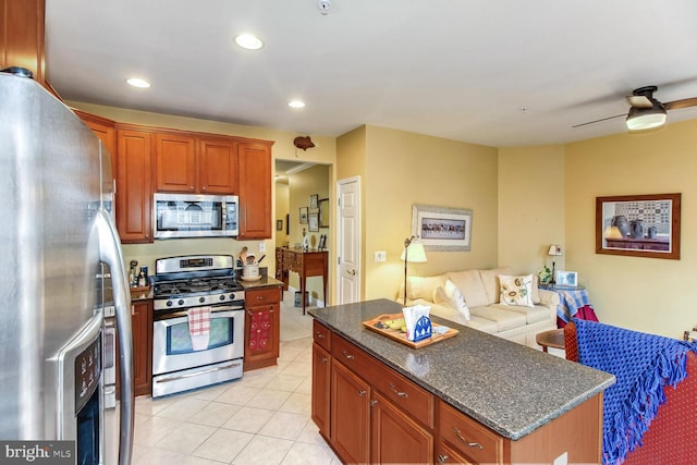 kitchen featuring ceiling fan, stainless steel appliances, light tile patterned floors, dark stone counters, and a kitchen island