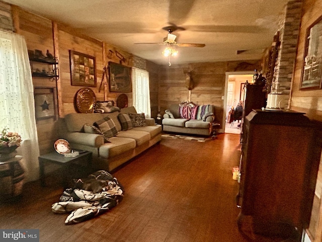 living room with a textured ceiling, dark hardwood / wood-style flooring, ceiling fan, and wood walls