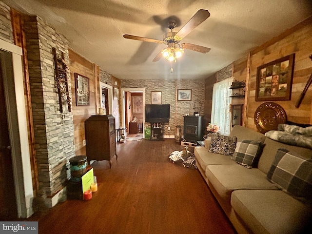 living room featuring a textured ceiling, ceiling fan, a wood stove, and dark wood-type flooring