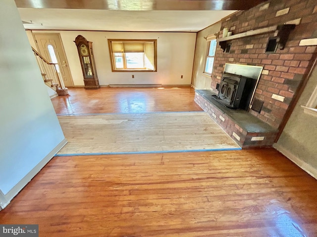 unfurnished living room with light hardwood / wood-style floors, a wood stove, and a healthy amount of sunlight