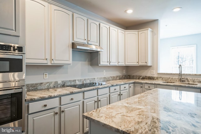 kitchen with light stone countertops, gray cabinetry, stainless steel double oven, black electric cooktop, and sink