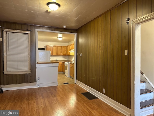 kitchen with wooden walls, light hardwood / wood-style flooring, and white appliances