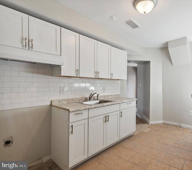 kitchen featuring light stone countertops, white cabinetry, sink, and tasteful backsplash