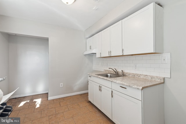 kitchen with backsplash, light stone counters, sink, light tile patterned floors, and white cabinetry