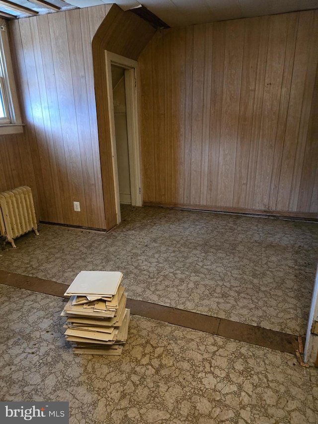 additional living space featuring wooden walls and radiator heating unit