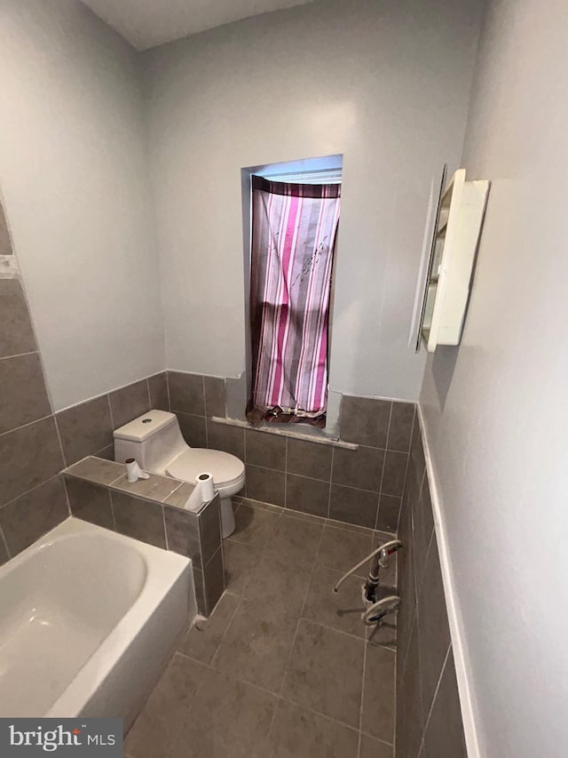 bathroom featuring tile patterned floors, a bath, toilet, and tile walls