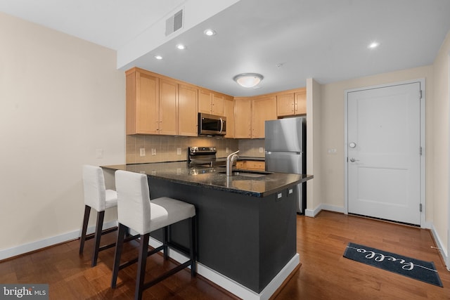 kitchen with kitchen peninsula, appliances with stainless steel finishes, decorative backsplash, light brown cabinets, and sink